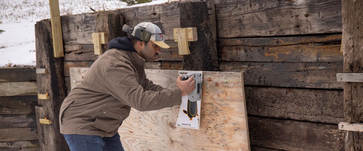 Guy tacking up a target against a wooden fence.