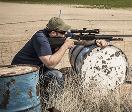 Man pointing rifle while resting in a barrel