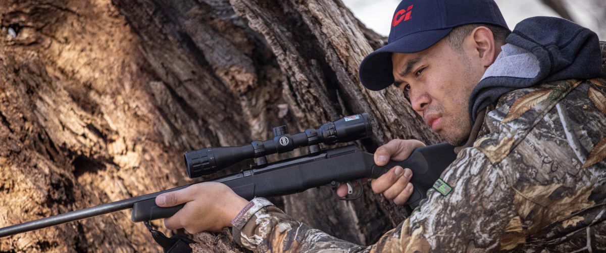 hunter shooting rifle around a tree