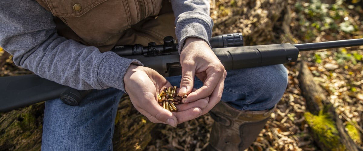 man holding CCI 22LR Cartridges in hand with rifle in lap