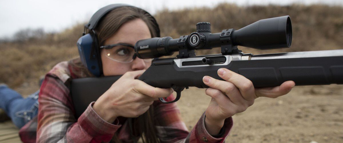 lady in a prone position looking down the scope of a rifle