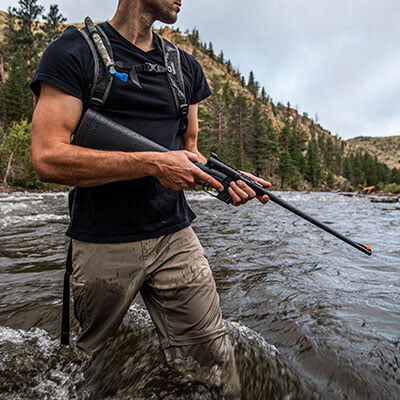 hunter carrying rifle while walking in the water