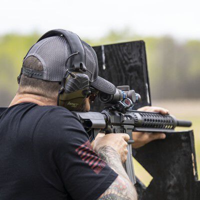 man aiming a rifle that is rested on a wood support