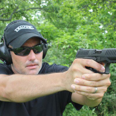 Man pointing pistol in front of row of trees