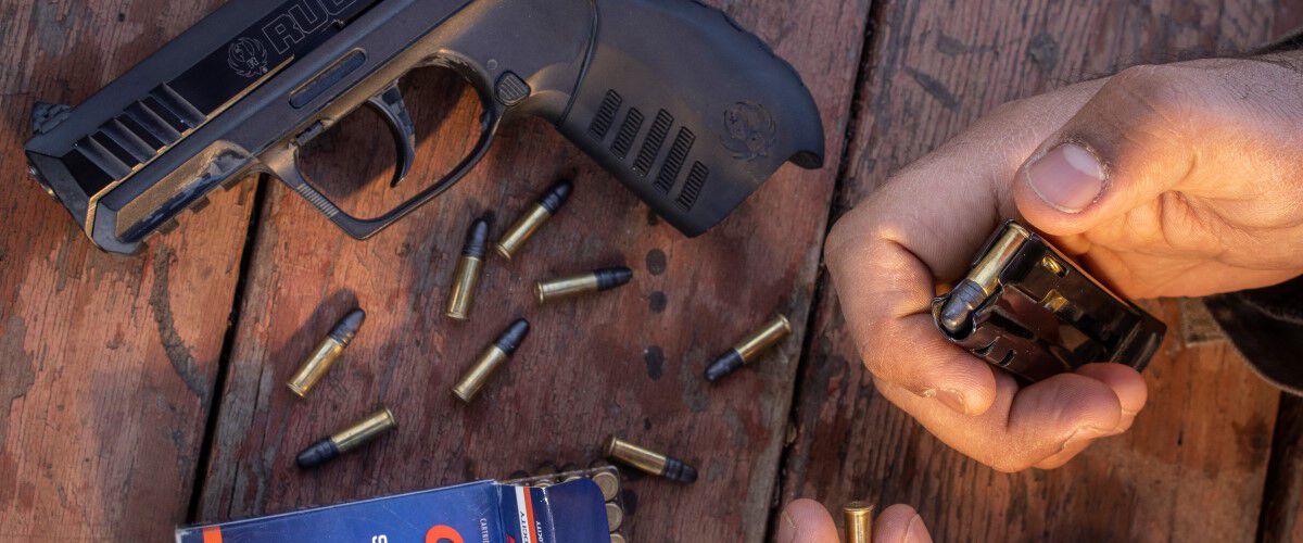 CCI cartridges being loaded into a magazine with other cartridges laying on a table with a pistol