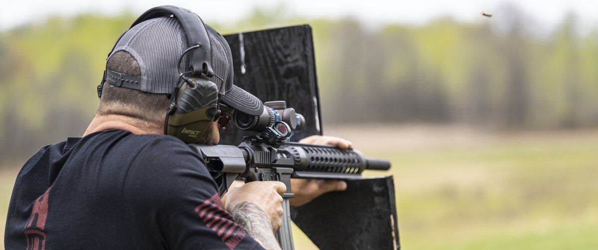 man aiming a rifle that is rested on a wood support