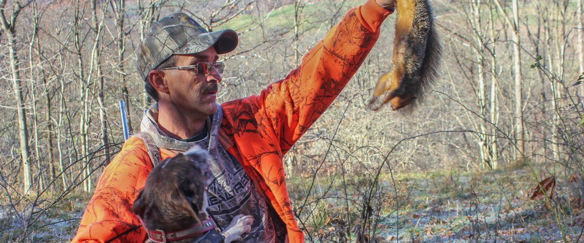 hunter with his dog holding up dead squirrel