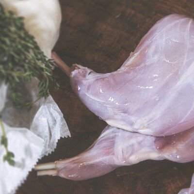 raw rabbit leg on a table beside from herbs