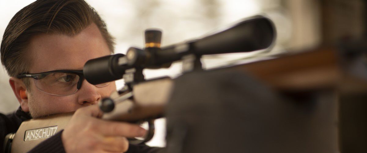 man looking down the scope of a resting rifle