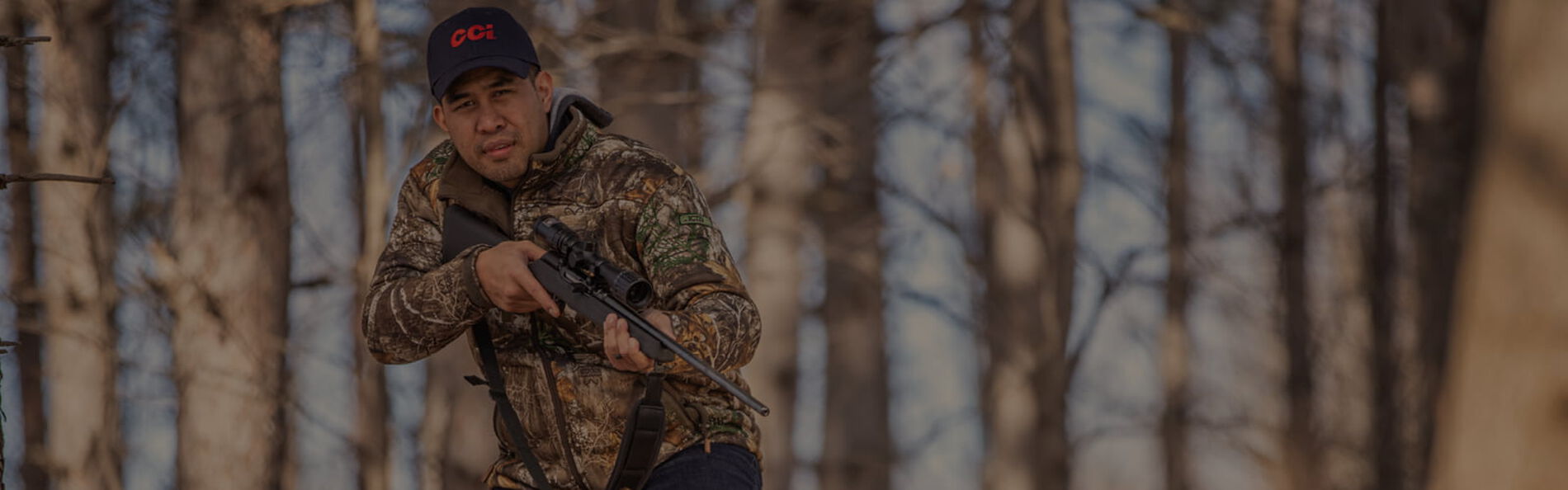 hunter holding rifle in front of a tree line