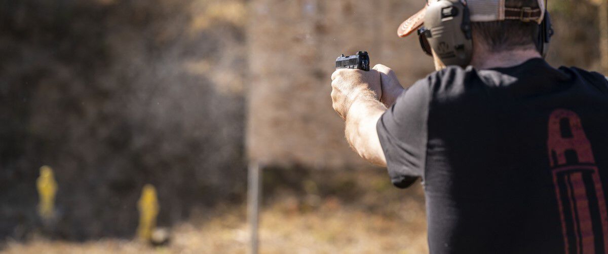 man pointing a handgun at a couple targets at an outdoor range