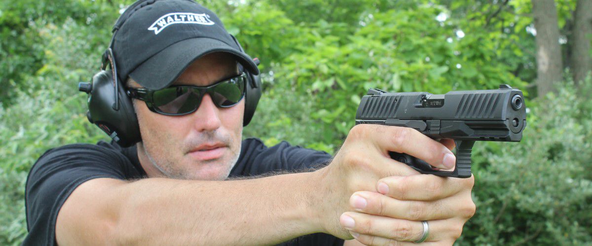 Man pointing pistol in front of row of trees