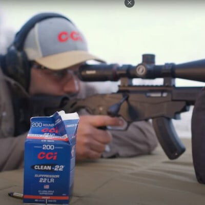 shooter looking down the scope of rifle resting on a table with a box of Clean-22