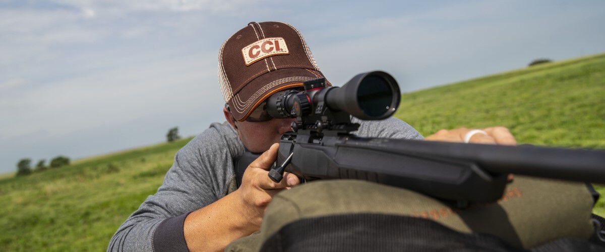 man looking down a rifle scope outside