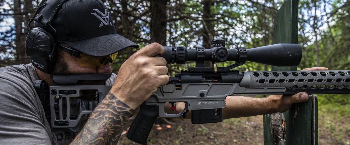 shooter looking down the scope of a rifle resting on a range obstacle