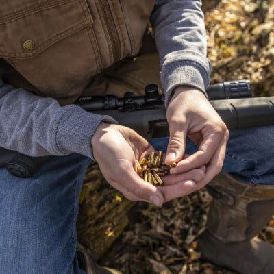 man holding CCI 22LR Cartridges in hand with rifle in lap