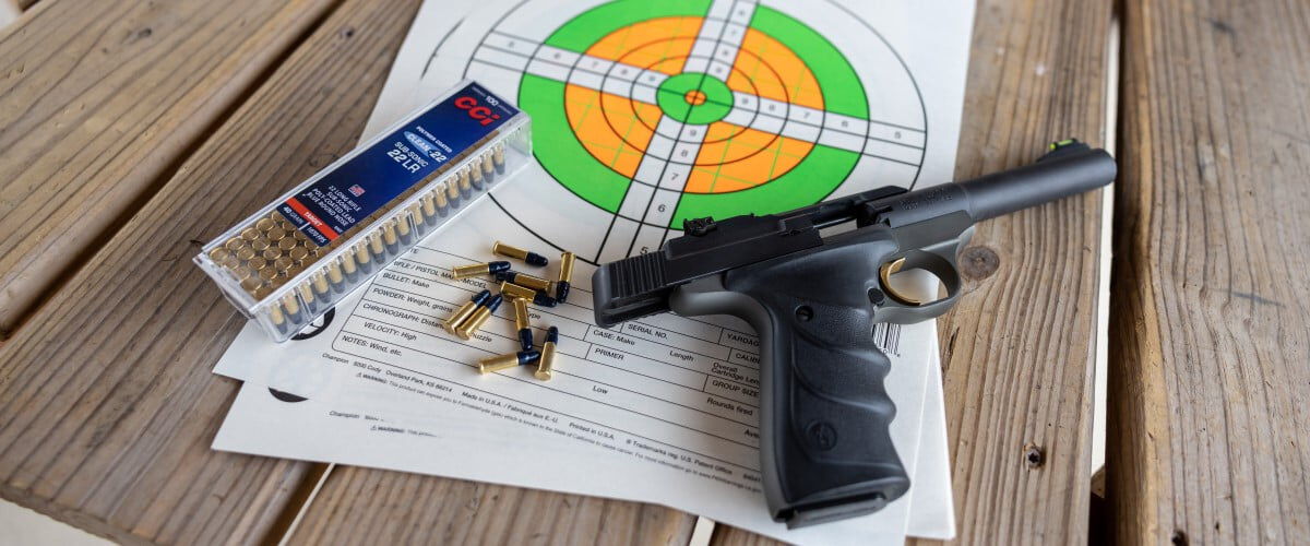 handgun with target, box of Subsonic and cartridges laying on a table