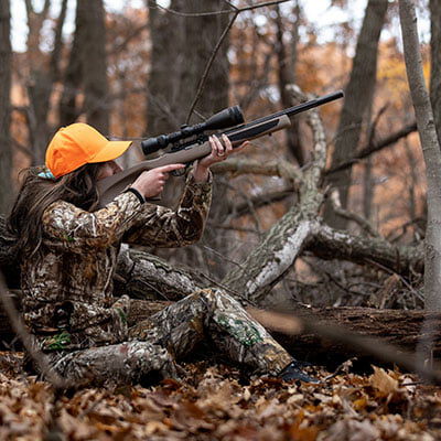 hunter aiming rifle in a wooded area